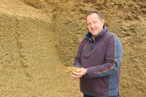 Alistair Channing standing with his back to a maize silage clamp. He is holding some maize silage in his cupped hands.