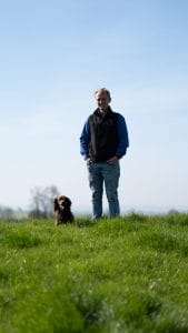 Tom and his dog stood in a field of grass.